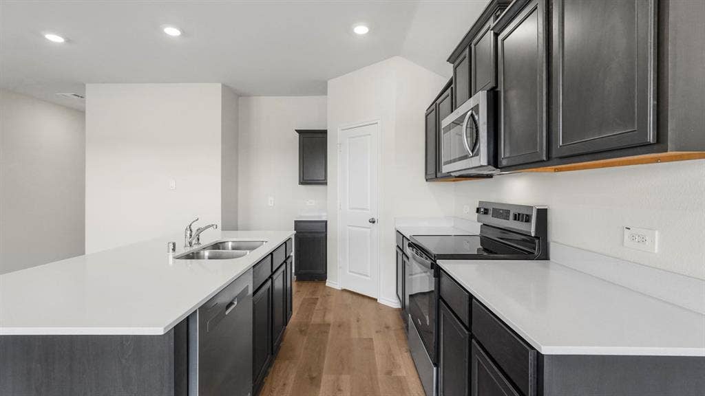 189 Brooks Street, Bullard, TX 75757 Kitchen featuring a double basin sink, stainless steel appliances, dark wood-finish cabinetry, light-toned countertops, and wood-finish flooring