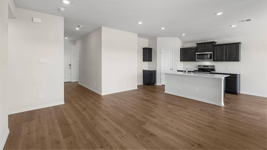 189 Brooks Street, Bullard, TX 75757 Spacious interior featuring wood-finish flooring, recessed lighting, a kitchen island with a sink, stainless steel appliances, and dark-stained cabinetry