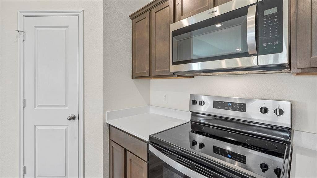 215 Yates Street, Bullard, TX 75757 Stainless steel microwave and electric range, dark wood-finish cabinetry, and solid surface countertop