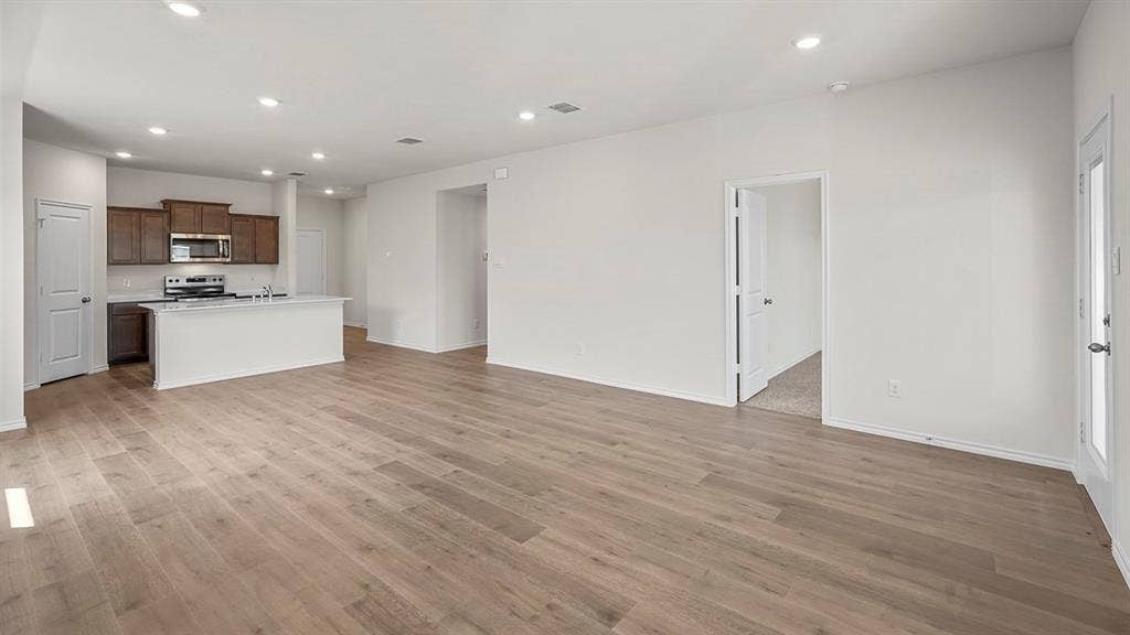 215 Yates Street, Bullard, TX 75757 Expansive open-concept living space featuring wood-finish flooring, recessed lighting, and a kitchen with dark wood cabinetry, stainless steel appliances, and a central island with a sink