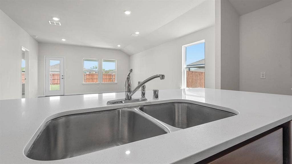 215 Yates Street, Bullard, TX 75757 White solid surface countertop with an undermount double basin sink and a chrome pull-down faucet