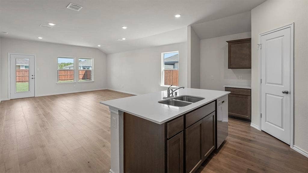 215 Yates Street, Bullard, TX 75757 Open-concept living space with wood-finish flooring, recessed lighting, white walls, and a kitchen island featuring a double-basin sink and white countertop