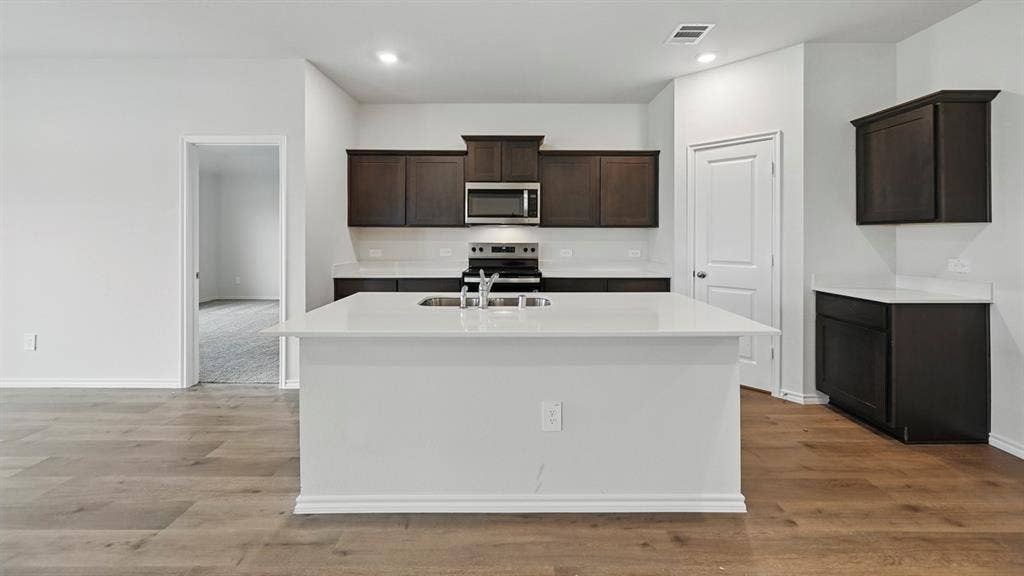 209 Yates Street, Bullard, TX 75757 Kitchen with wood-finish flooring, dark wood cabinetry, white countertops, and a large central island featuring a stainless steel sink