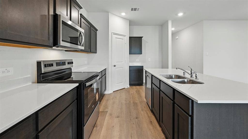 209 Yates Street, Bullard, TX 75757 Kitchen featuring wood-finish flooring, dark cabinetry, light countertops, stainless steel appliances, and a double basin sink