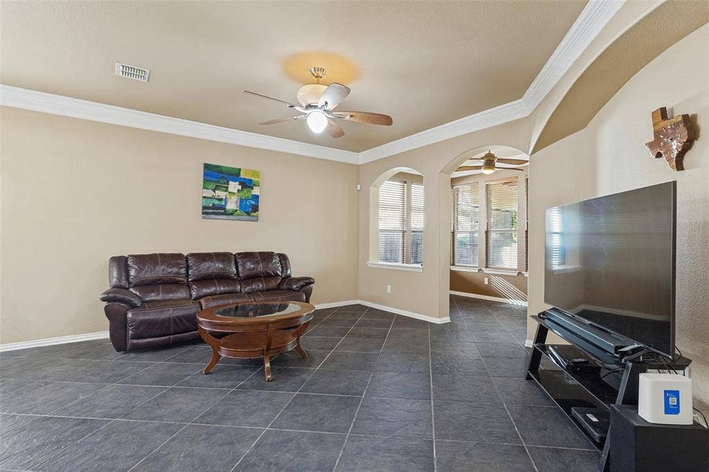 Tile flooring, crown molding, arched doorways, and ceiling fan.