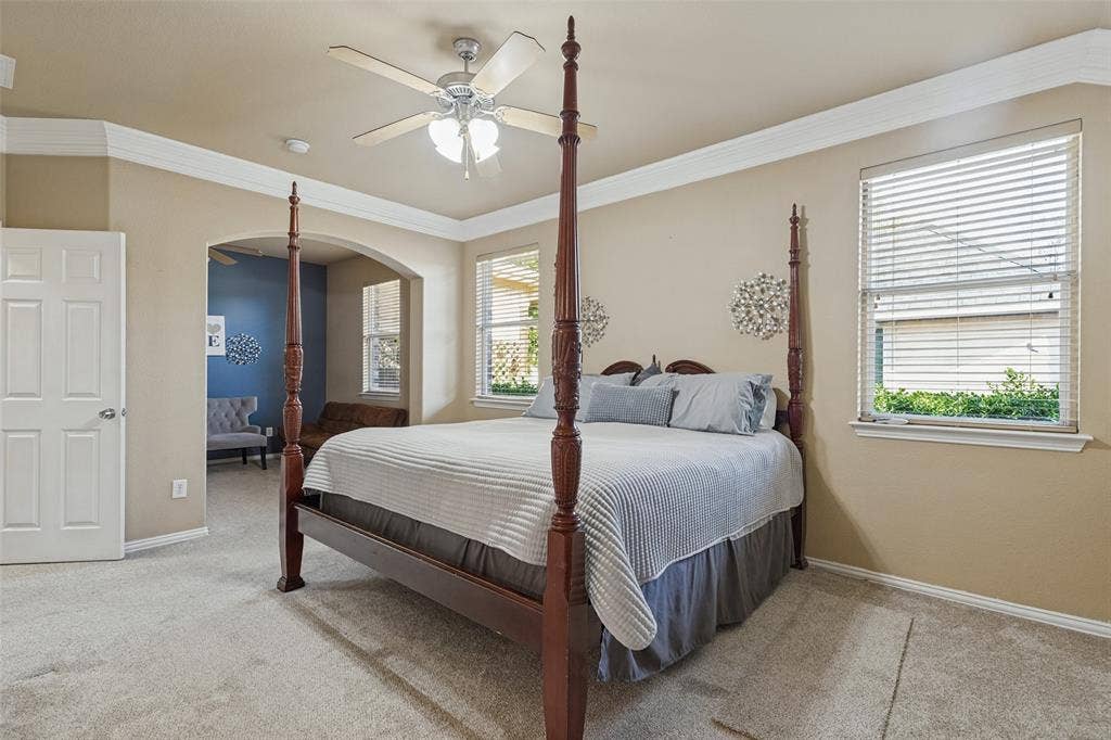 Neutral tone wall paint, crown molding, arched doorway, ceiling fan with integrated lighting, and carpeted flooring