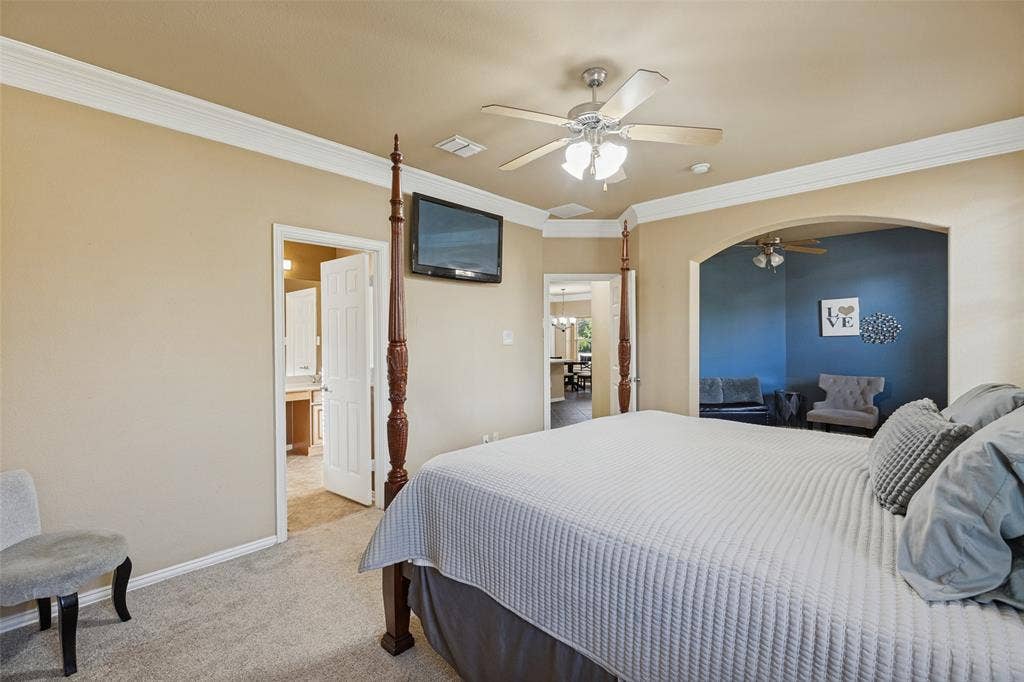 Carpeted room with a ceiling fan, crown molding, and an arched opening to bonus room