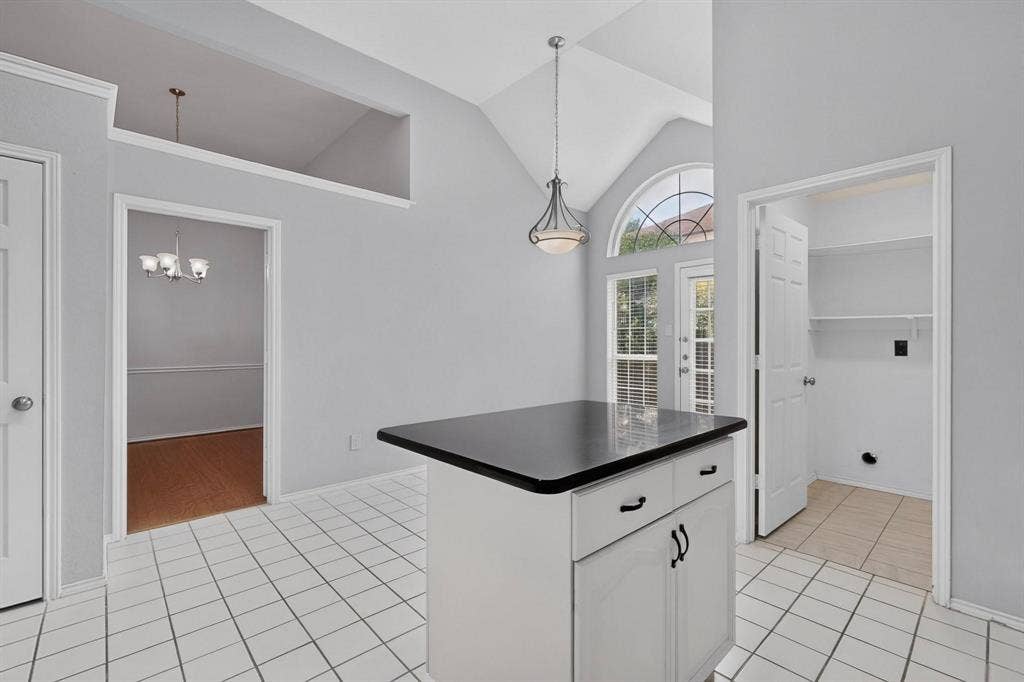 2702 Garden Springs Drive, Richardson, TX 75082 Vaulted ceiling with an arched window, white tile flooring, white cabinetry island with black countertop, and an exterior door with integrated blinds