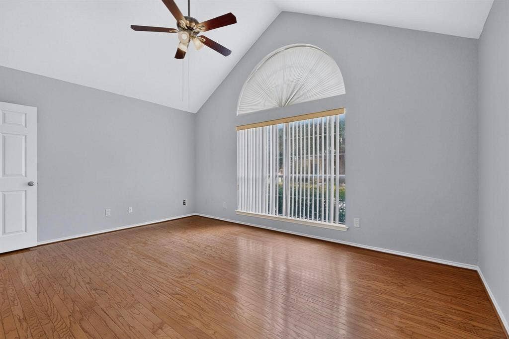 2702 Garden Springs Drive, Richardson, TX 75082 Vaulted ceiling with a ceiling fan, arched transom window, large window with vertical blinds, wood-finish flooring, and a paneled door