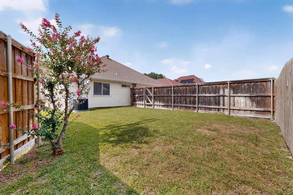 2702 Garden Springs Drive, Richardson, TX 75082 Fenced backyard featuring a manicured lawn, established tree, and a home exterior with a visible window