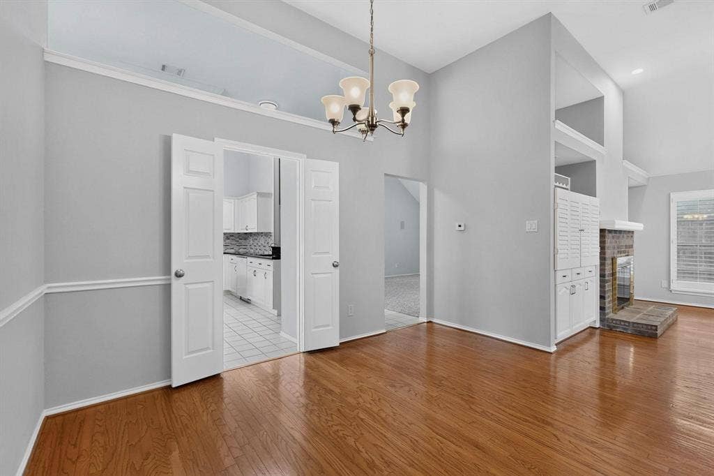 2702 Garden Springs Drive, Richardson, TX 75082 Vaulted ceilings with a chandelier, wood-finish flooring, white double French doors, and a brick fireplace