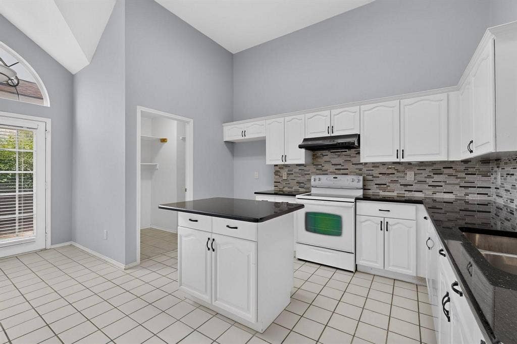 2702 Garden Springs Drive, Richardson, TX 75082 Kitchen featuring vaulted ceilings, white cabinetry, dark countertops, a tiled backsplash, and a central island
