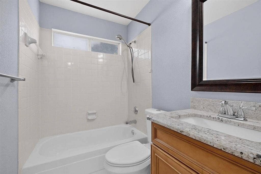 2702 Garden Springs Drive, Richardson, TX 75082 Bathroom featuring a white bathtub, tiled shower surround, frosted window, wood-finish vanity, and speckled countertop