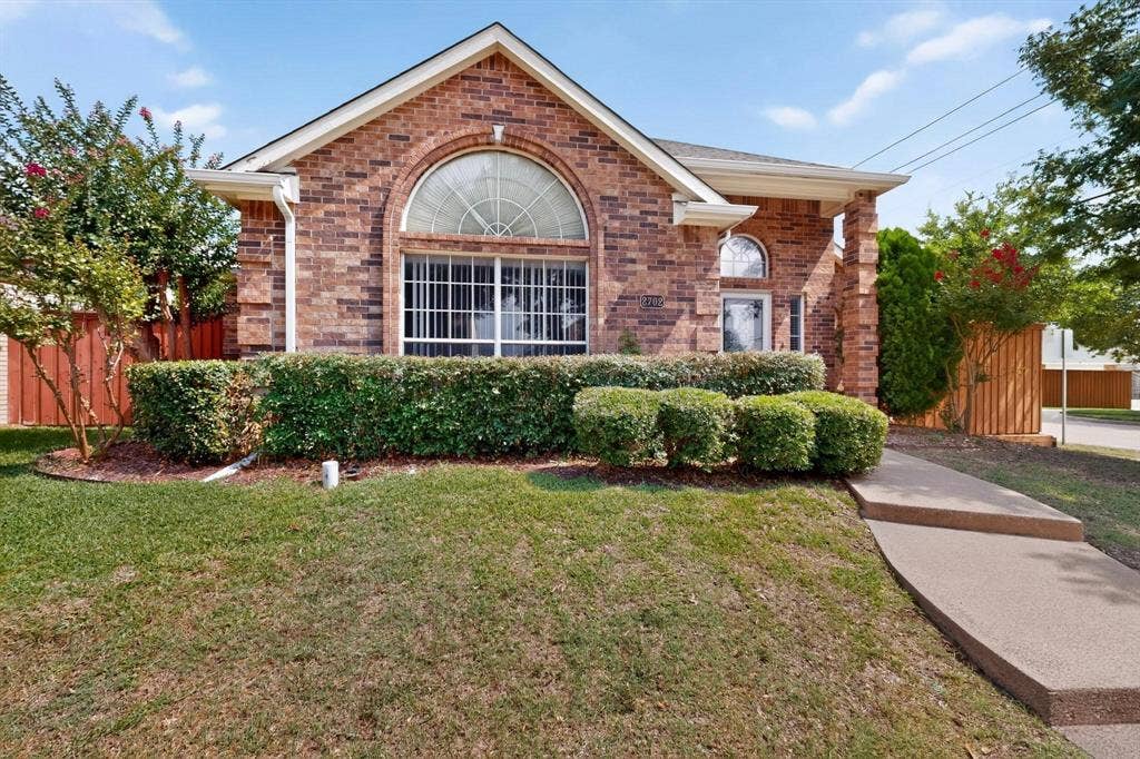 2702 Garden Springs Drive, Richardson, TX 75082 Brick exterior with an arched window, a covered entryway, and mature landscaping