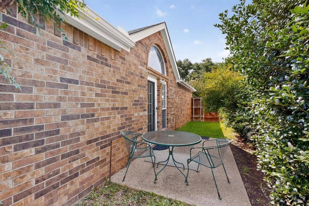2702 Garden Springs Drive, Richardson, TX 75082 Brick exterior with white gutters, arched window above a glass-paned door, concrete patio, and fenced yard