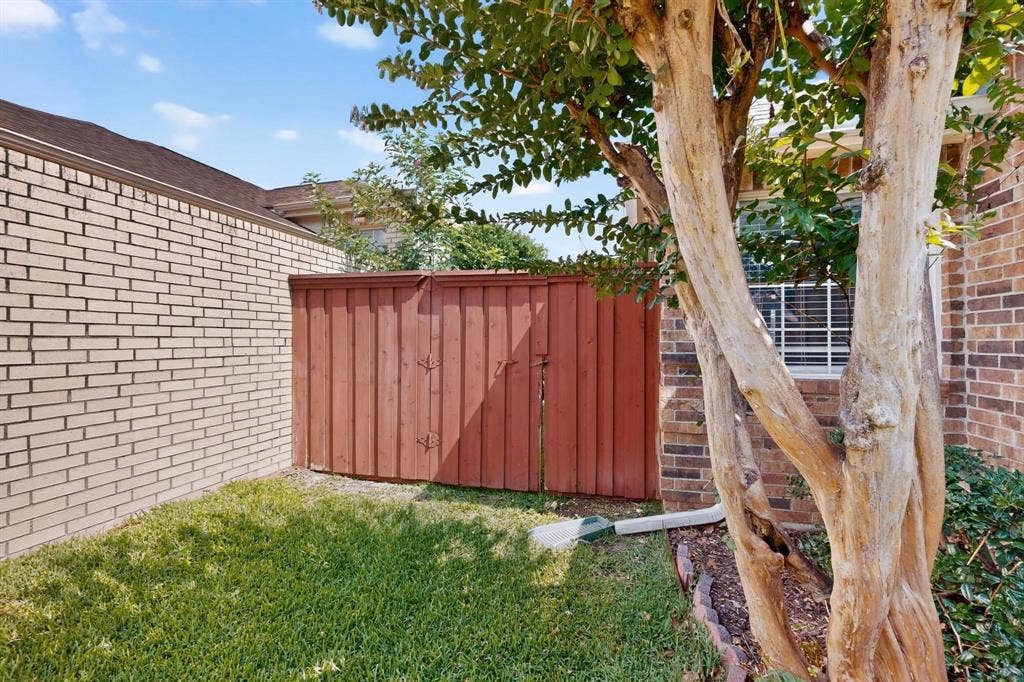 2702 Garden Springs Drive, Richardson, TX 75082 Brick exterior featuring a wood fence, established tree, and green lawn
