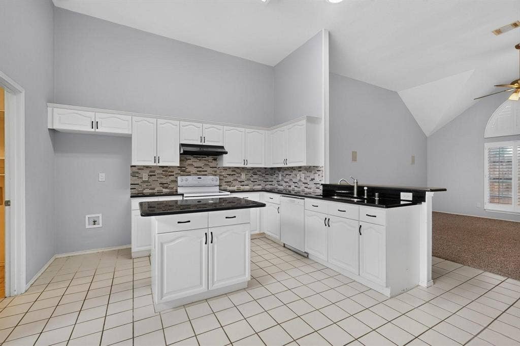 2702 Garden Springs Drive, Richardson, TX 75082 Kitchen featuring white cabinetry, black countertops, a central island, and a tiled backsplash
