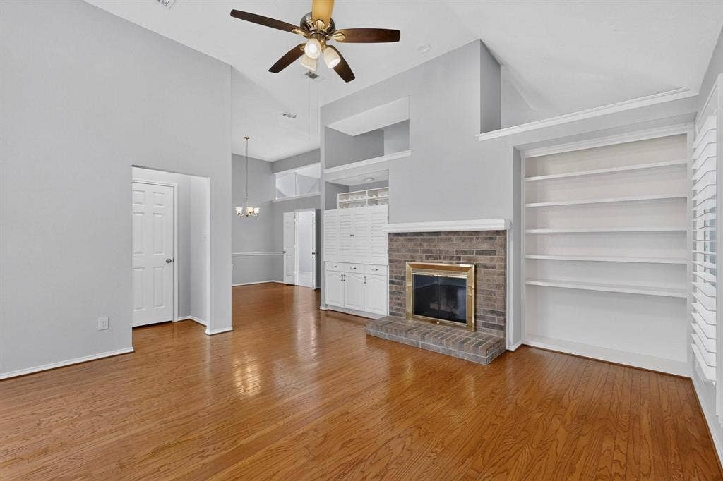 2702 Garden Springs Drive, Richardson, TX 75082 Vaulted ceiling with a ceiling fan, wood-finish flooring, brick fireplace with a brass-tone insert, built-in shelving, and built-in white cabinetry