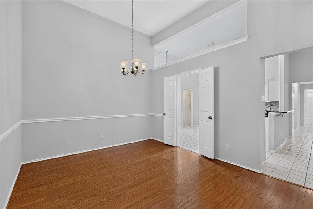 2702 Garden Springs Drive, Richardson, TX 75082 Vaulted ceiling with an attached chandelier, wood-finish flooring, wainscoting, and white bi-fold doors