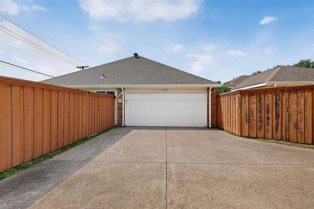 2702 Garden Springs Drive, Richardson, TX 75082 Attached two-car garage with a concrete driveway and brick exterior detailing