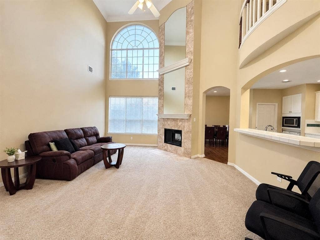10316 Donley Drive, Irving, TX 75063 Two-story living area featuring a prominent arched window, fireplace with stone surround, and ceiling fan