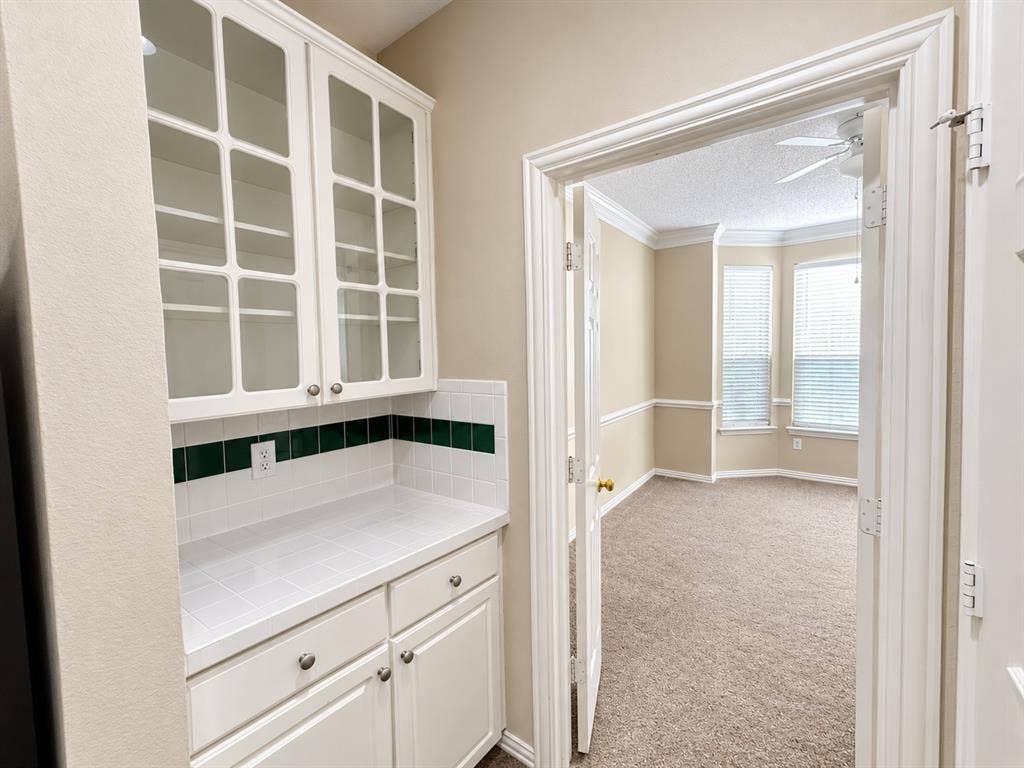 10316 Donley Drive, Irving, TX 75063 Built-in cabinetry with glass-front uppers and lower storage, tiled countertop, and a decorative tile backsplash