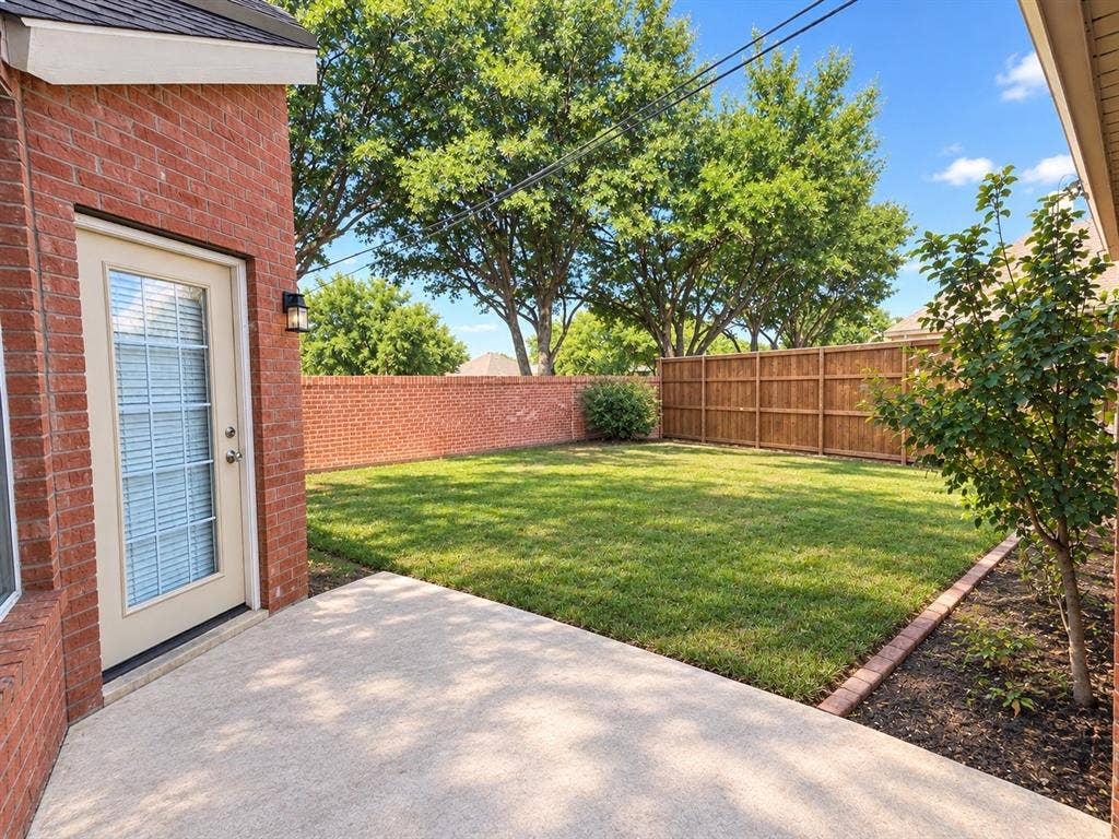 10316 Donley Drive, Irving, TX 75063 Private backyard featuring a concrete patio, brick exterior, wood fence, and mature trees