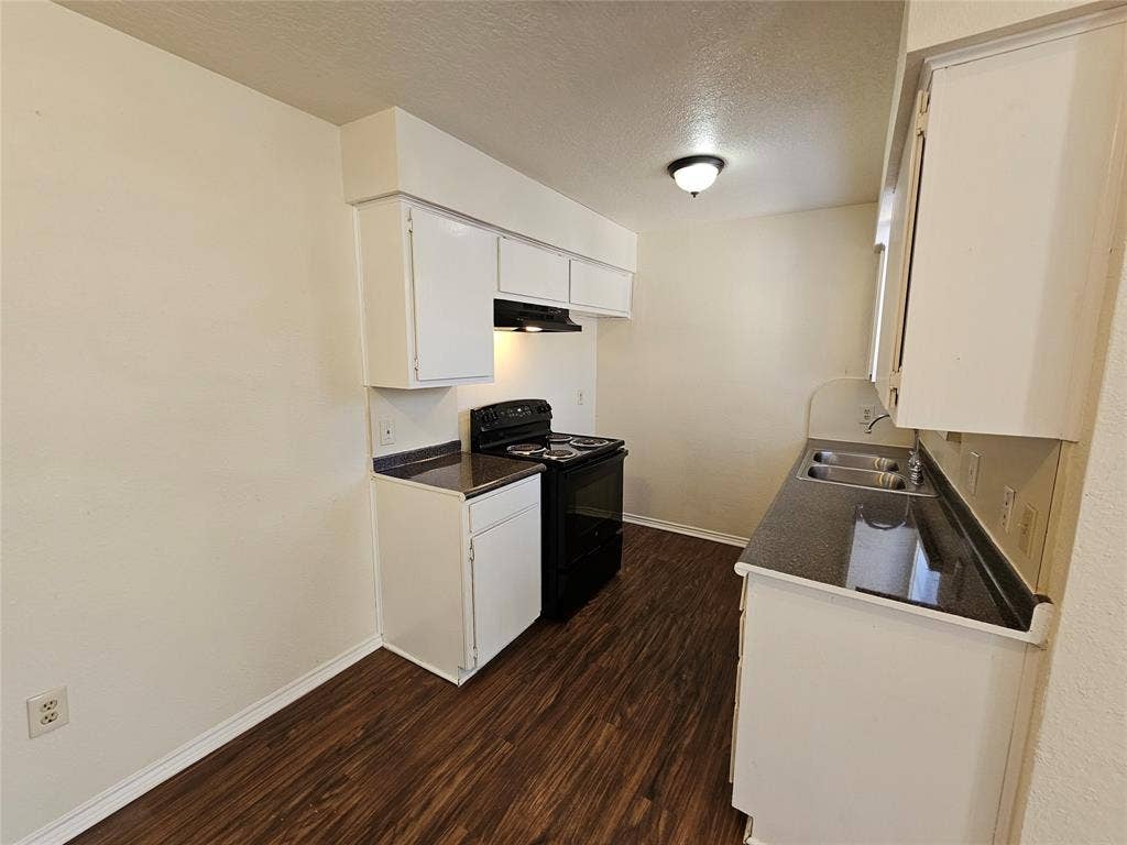 Kitchen with white cabinetry, dark countertops, a black range, and wood-finish flooring