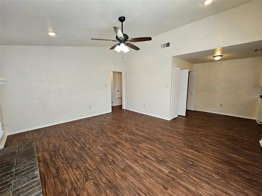 Expansive interior featuring wood-finish flooring, vaulted ceilings, and a ceiling fan with integrated lighting