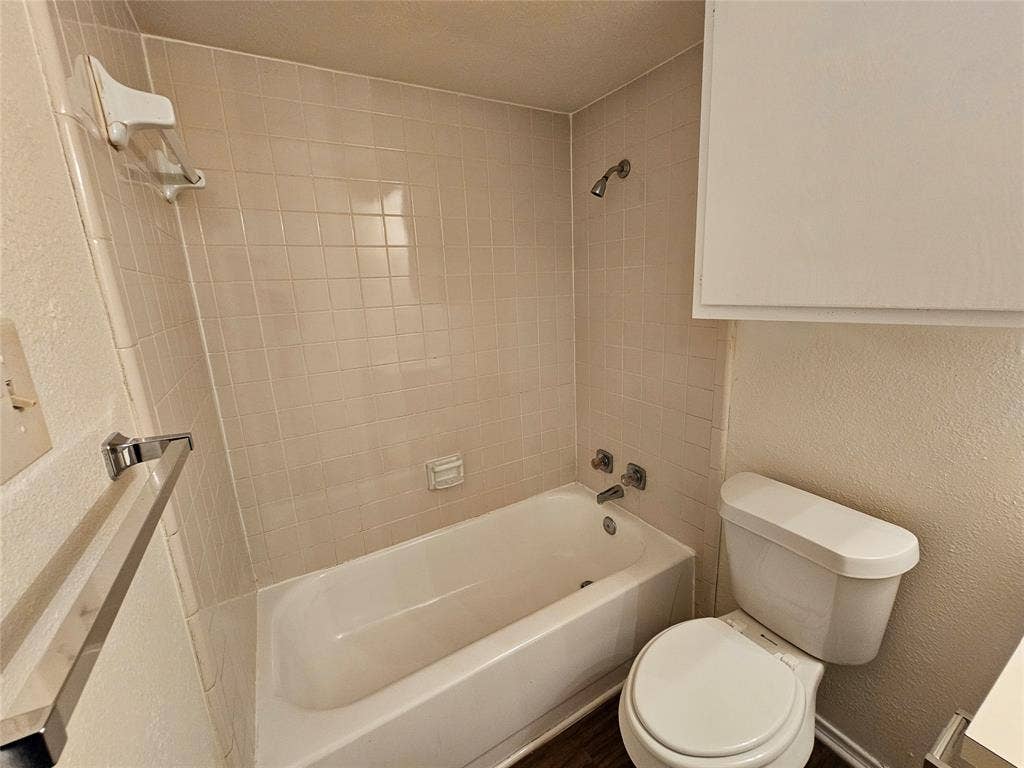 Bathtub with tiled surround, shower fixture, and wall-mounted storage cabinet