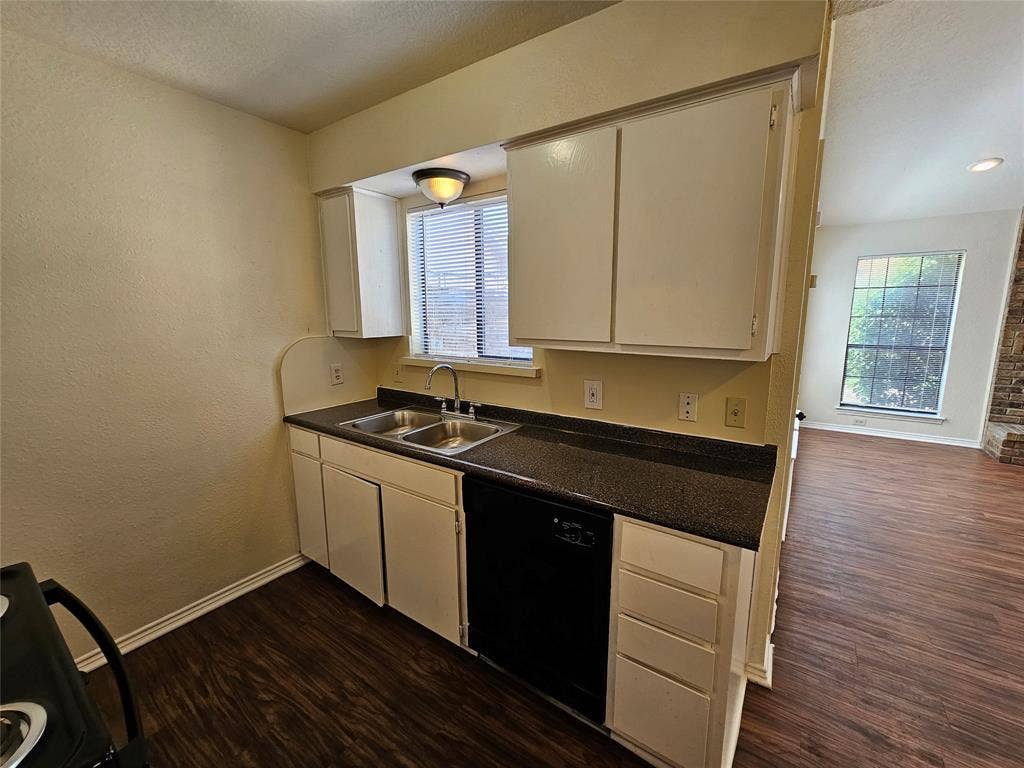 Kitchen featuring white cabinetry, double basin sink, dark countertop, and integrated dishwasher