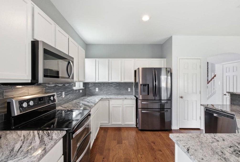 White cabinetry, stainless steel appliances, wood-finish flooring, stone countertops, and a tiled backsplash