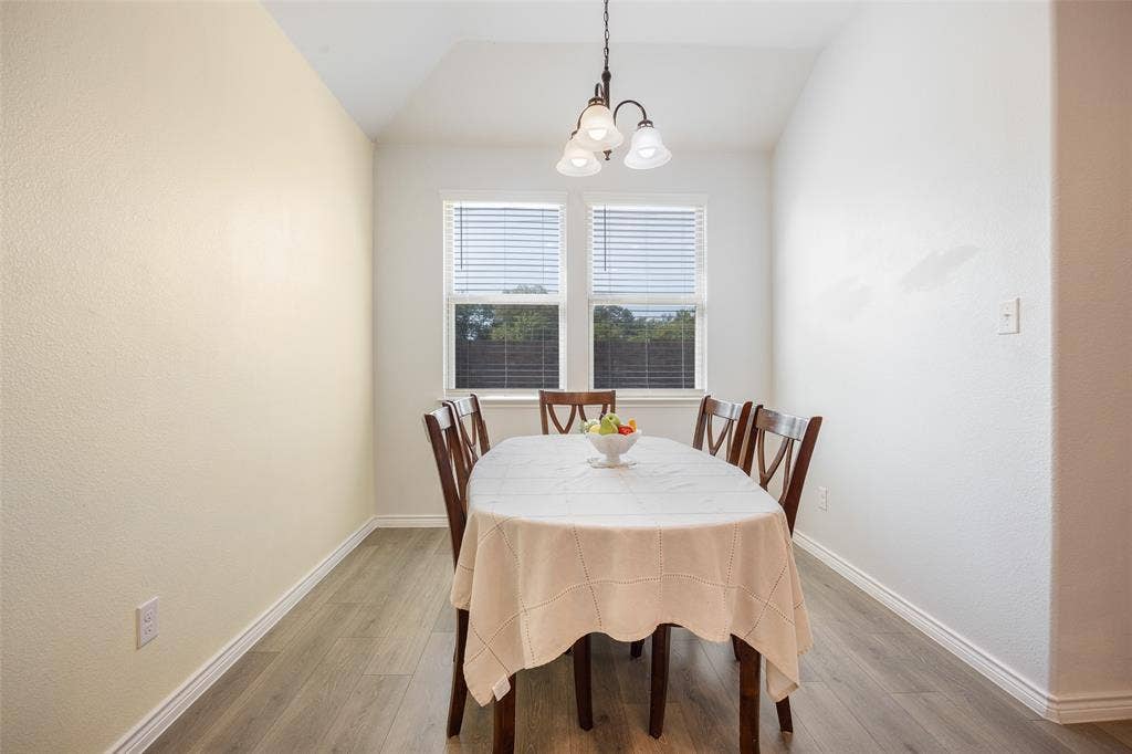 1101 Crepe Myrtle Lane, Anna, TX 75409 Vaulted ceiling with an attached chandelier, two windows with blinds, and wood-finish flooring