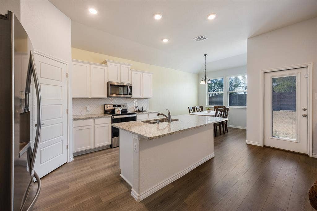 1101 Crepe Myrtle Lane, Anna, TX 75409 Kitchen featuring white cabinetry, stainless steel appliances, a center island with a sink, and wood-finish flooring