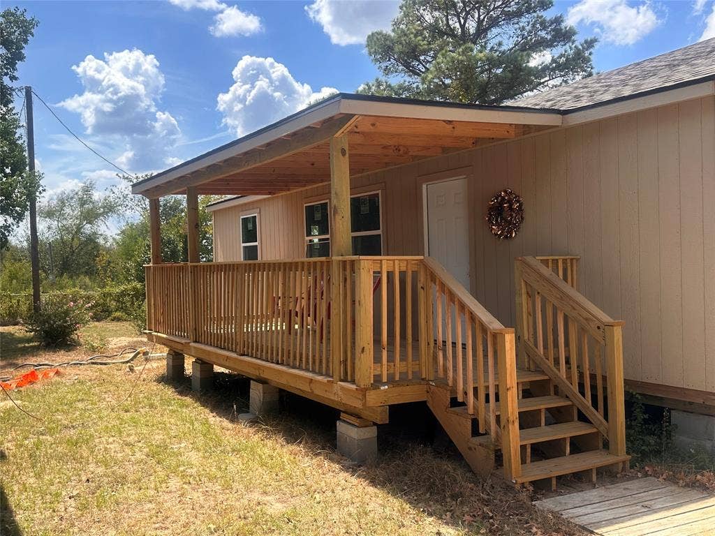 13601 Woodridge, Eustace, TX 75124 Covered front porch with wood-finish decking and railing, light-colored vertical siding, and a white entry door