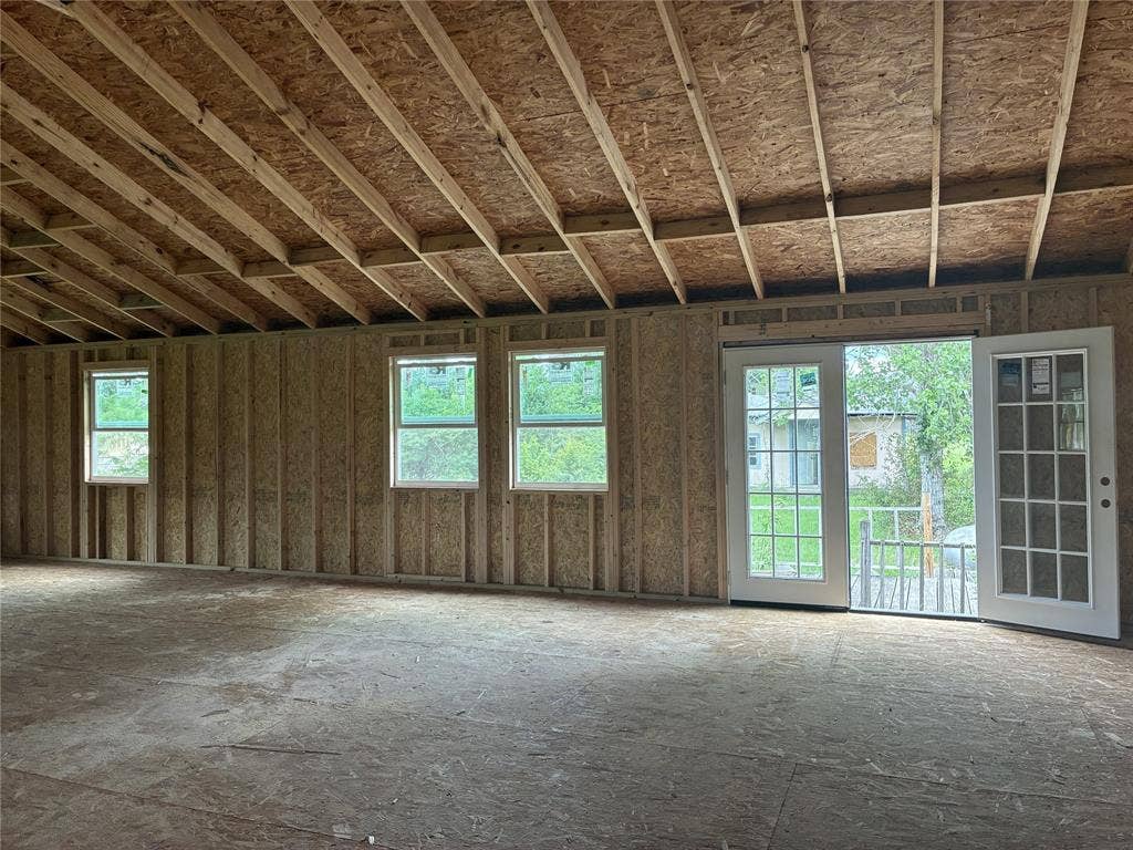13601 Woodridge, Eustace, TX 75124 Unfinished interior framing with exposed ceiling joists, multiple windows, and a double-door exterior entry