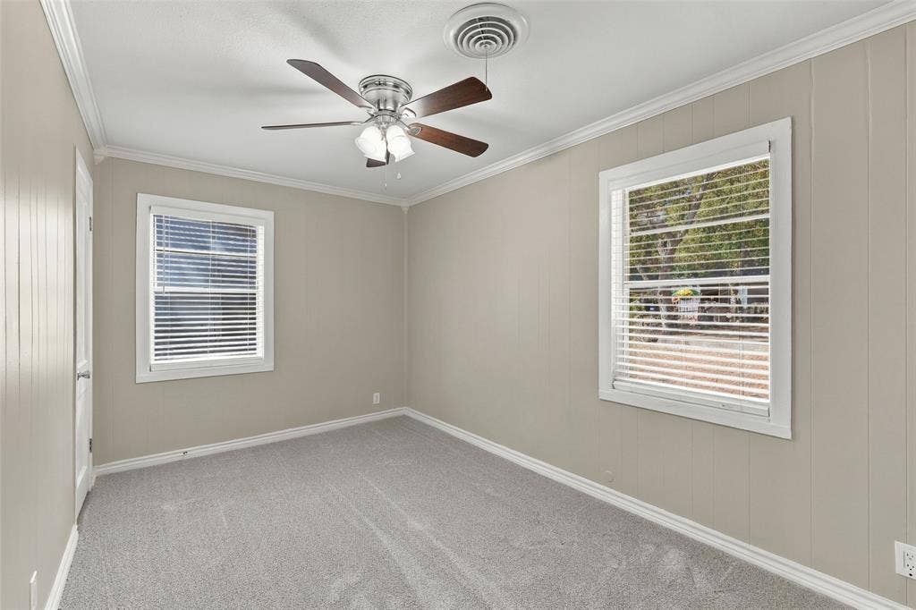 605 NE 33rd Street, Grand Prairie, TX 75050 Carpeted room featuring two windows, crown molding, and a ceiling fan with integrated lighting