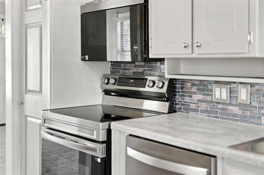 605 NE 33rd Street, Grand Prairie, TX 75050 Stainless steel oven with a smooth cooktop, coordinating microwave, mosaic tile backsplash, light-toned countertops, and white upper cabinetry