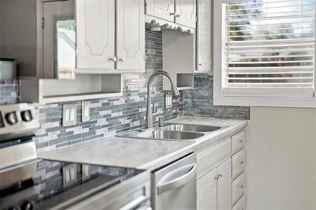 605 NE 33rd Street, Grand Prairie, TX 75050 White cabinetry, dual-basin stainless steel sink, and patterned tile backsplash