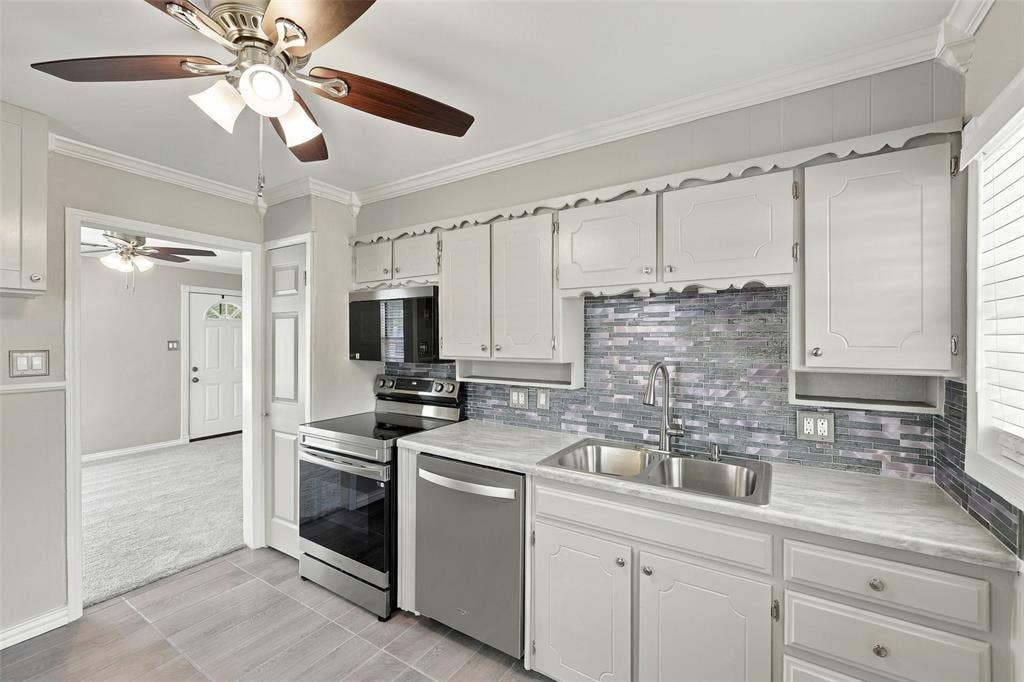 605 NE 33rd Street, Grand Prairie, TX 75050 White cabinetry with crown molding, stainless steel appliances, stone-look countertops, and a mosaic tile backsplash