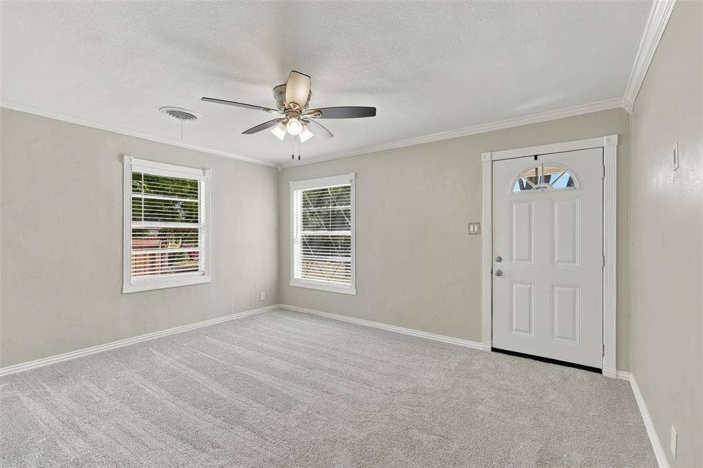 605 NE 33rd Street, Grand Prairie, TX 75050 Light gray wall paint, two windows with blinds, a ceiling fan with integrated lighting, and a white paneled entry door with an arched glass insert