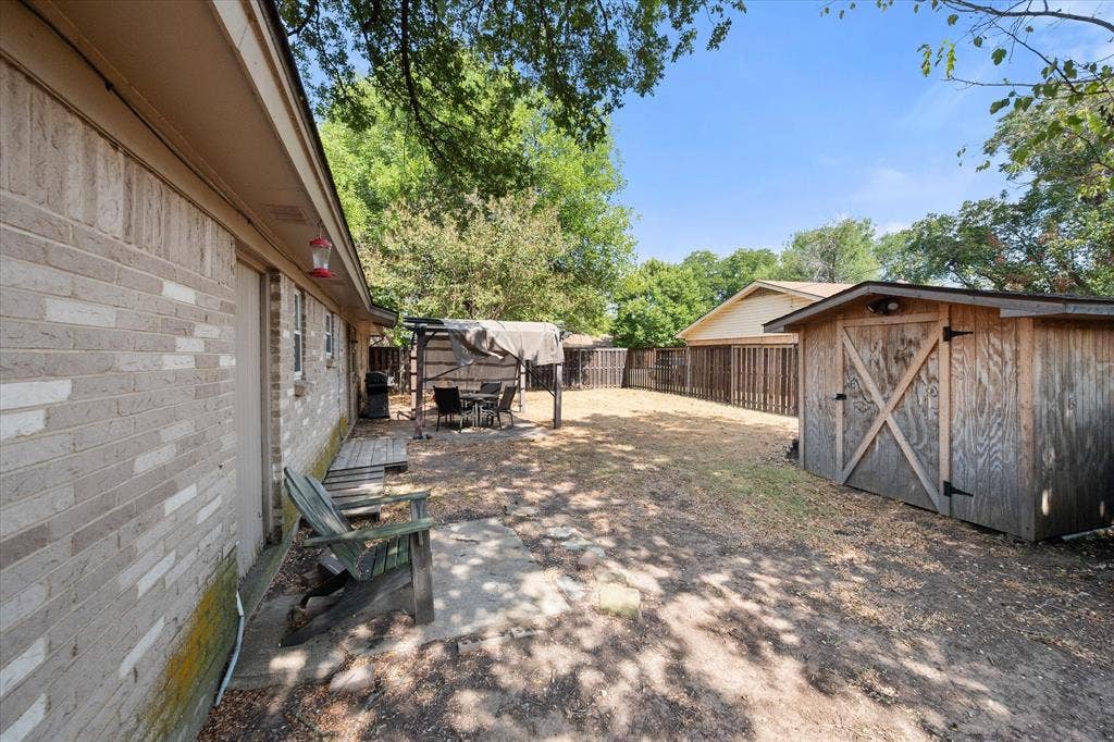 144 Jill Ann Drive, Burleson, TX 76028 Expansive backyard featuring a wood storage shed, privacy fencing, and a covered outdoor patio area