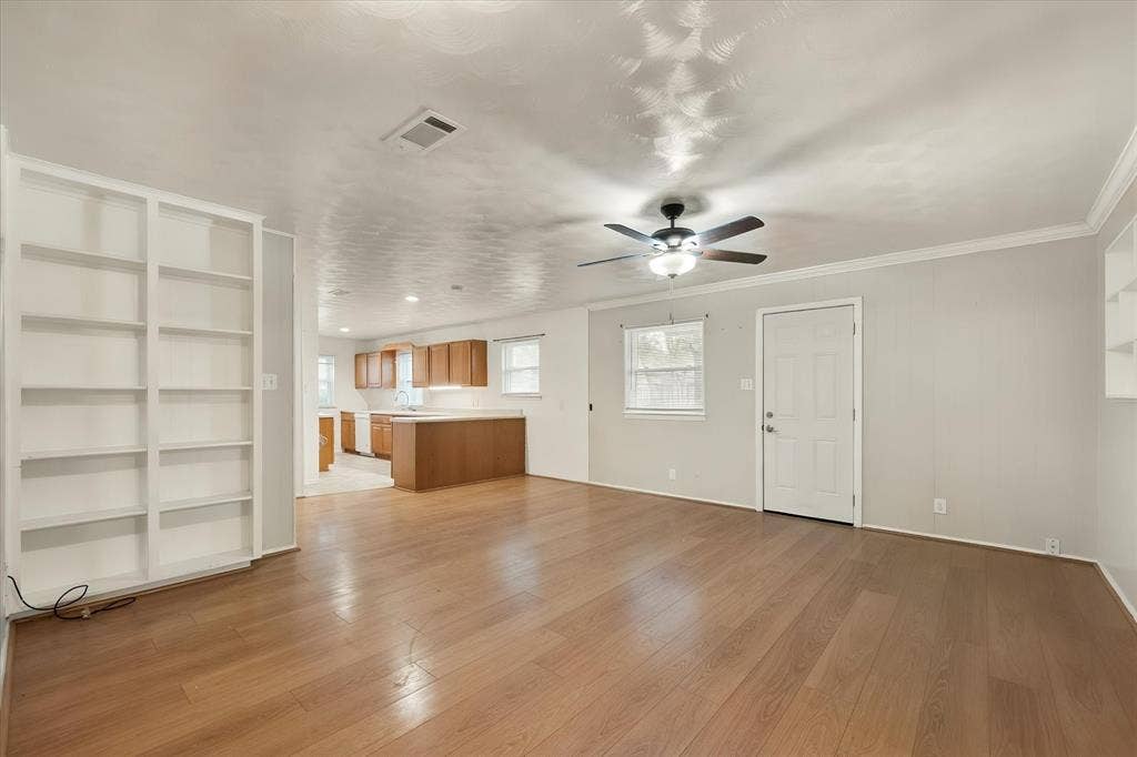 144 Jill Ann Drive, Burleson, TX 76028 Open-concept living space featuring wood-finish flooring, built-in shelving, a ceiling fan, and crown molding