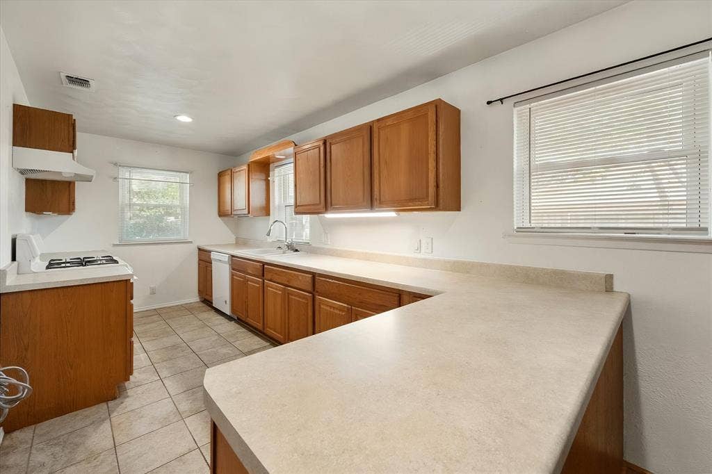 144 Jill Ann Drive, Burleson, TX 76028 Kitchen featuring wood-finish cabinetry, solid surface countertops, a gas range, dishwasher, and tile flooring