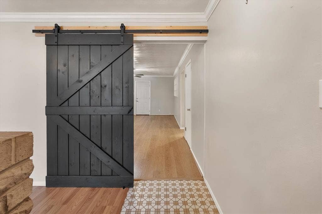 144 Jill Ann Drive, Burleson, TX 76028 Black barn door with exposed rail hardware, wood-finish flooring, and crown molding