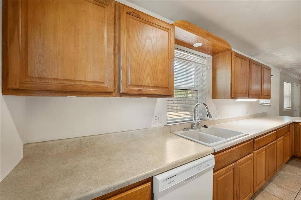 144 Jill Ann Drive, Burleson, TX 76028 Kitchen featuring wood cabinetry, light-toned countertops, a double basin sink with a chrome faucet, under-cabinet lighting, and a built-in dishwasher