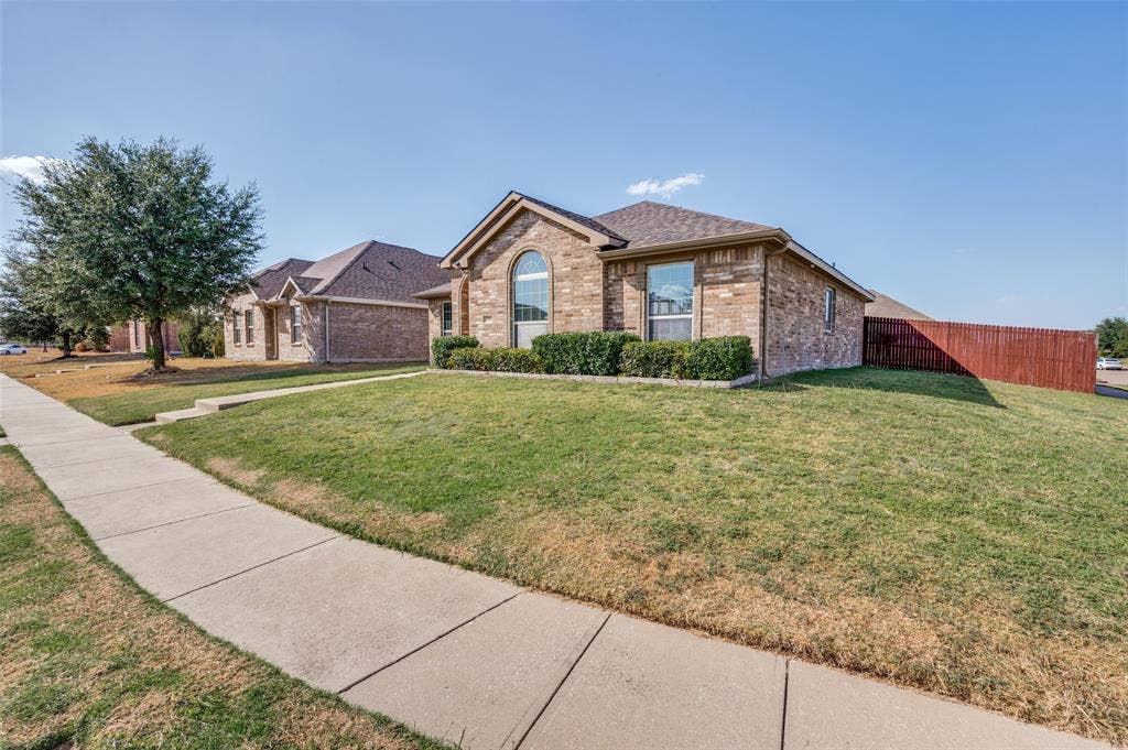 1929 Day Break Drive, Lancaster, TX 75146 Brick exterior with an arched window, landscaped shrubbery, and a concrete sidewalk