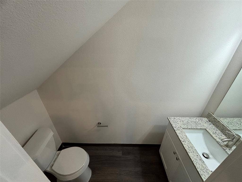 White vanity with a speckled countertop, a rectangular undermount sink, and wood-finish flooring
