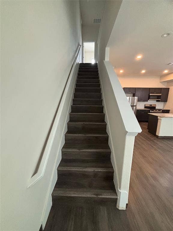 Staircase featuring wood-finish treads and risers, a white handrail, and white newel posts