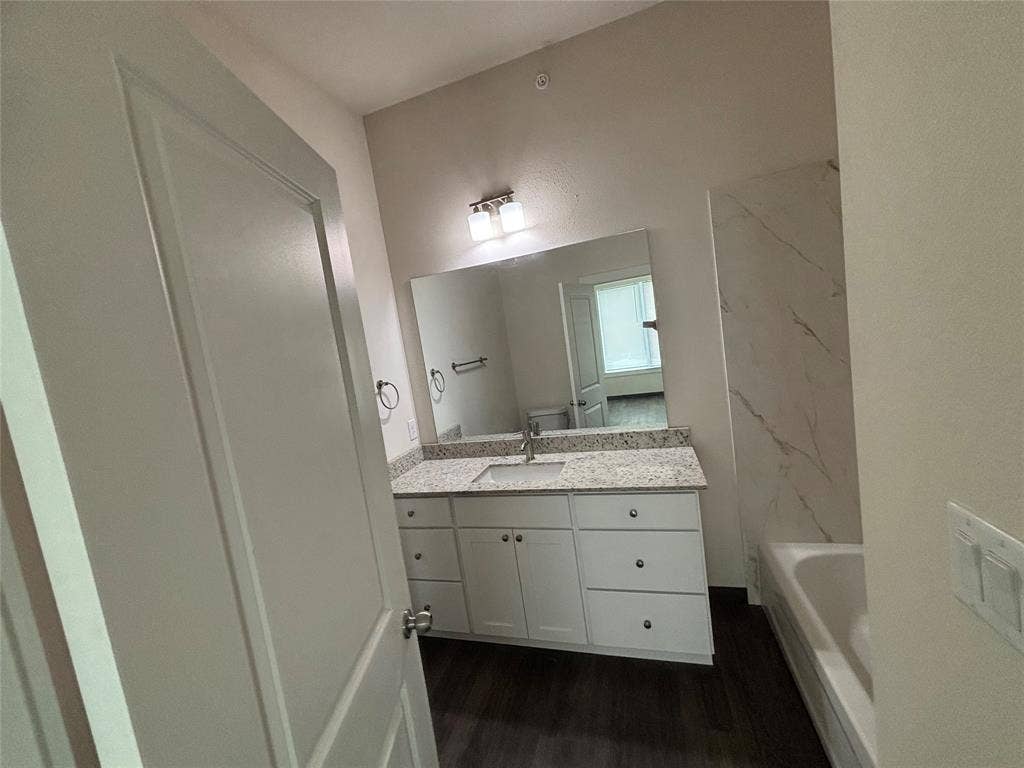 Bathroom featuring a single vanity with stone-finish countertop, white cabinetry, undermount sink, and wood-finish flooring